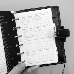 Peut inclure: Une image en noir et blanc d'un agenda quotidien avec un suivi de 31 jours. L'agenda a un onglet intitulé "Journal". L'agenda a une section pour la date, la description et la récompense. L'agenda a une section pour chaque jour du mois. L'agenda a une section pour chaque semaine du mois. L'agenda a une section pour chaque mois de l'année. L'agenda a une section pour chaque année. L'agenda a une section pour chaque décennie. L'agenda a une section pour chaque siècle. L'agenda a une section pour chaque millénaire.