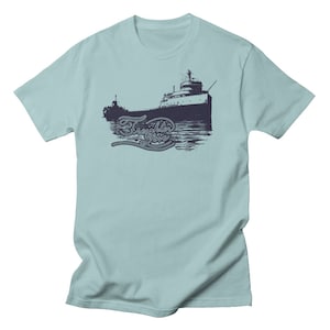 May include: A light blue t-shirt with a navy blue image of a freighter ship on the front. The ship is sailing on water and the text "Freighter Life" is written in a cursive font below the ship.