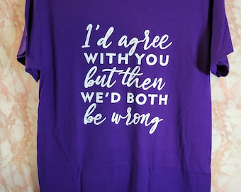 Op de afbeelding: Een paars Gildan t-shirt met de tekst "I'd agree with you but then we'd both be wrong" in witte letters. Het shirt hangt aan een zwarte hanger tegen een lichtroze en witte marmeren achtergrond.