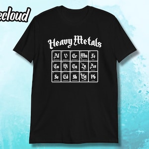 Op de afbeelding: Zwart T-shirt met witte tekst die "Heavy Metals" zegt en een tabel met chemische symbolen en namen voor zware metalen.