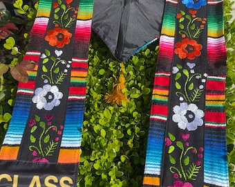 May include: A black graduation sash with colorful stripes and embroidered flowers. The sash has the text "CLASS OF" on both ends.