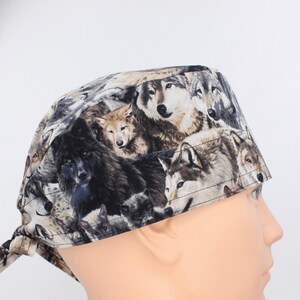 May include: A black and brown patterned surgical scrub hat with a wolf print. The hat has a tie at the back.