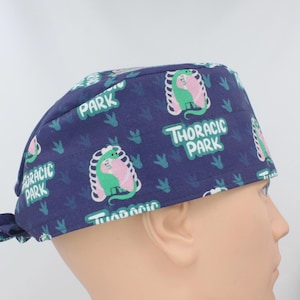 May include: A blue surgical scrub hat with a dinosaur print and the text "Thoracic Park".