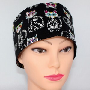 Puede incluir:  gorro de quir&oacute;fano negro con un patr&oacute;n de gato colorido del D&iacute;a de los Muertos. El gato tiene un dise&ntilde;o de esqueleto y detalles florales.