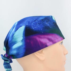 Può includere: Una cuffia chirurgica con una vivace stampa galassia nei toni del blu profondo, viola e verde acqua. Il tessuto presenta un motivo a cielo stellato con nuvole nebulose. La cuffia include una chiusura a laccio con nastri in tessuto abbinati.
