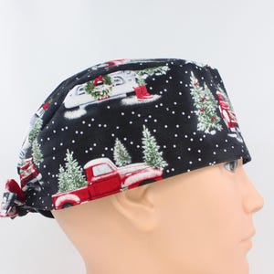 May include: A black scrub cap featuring a festive holiday pattern with red pickup trucks carrying green Christmas trees, white snowflakes, and wreaths. The fabric head covering has a tie-back closure and a contoured fit for secure wear.