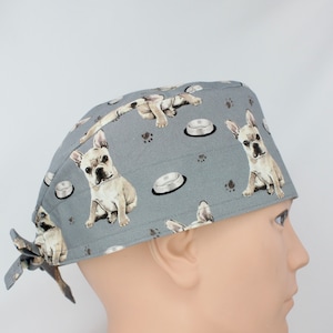 Può includere: Cappello da lavoro grigio con un motivo di bulldog francesi bianchi e ciotole per cani. Il cappello ha una cravatta sul retro.