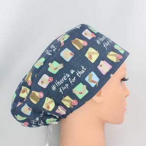 May include: A dark blue surgical scrub cap with a repeating pattern of colorful arm illustrations and the text "#there's a flap for that". The cap is designed to cover the hair during medical procedures.