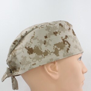 Peut inclure: Une charlotte de bloc opératoire avec un motif camouflage numérique dans des tons beige, sable et marron. Ce couvre-chef présente une bande frontale structurée et un système de nouage à l'arrière, fabriqué dans un tissu à texture tissée.
