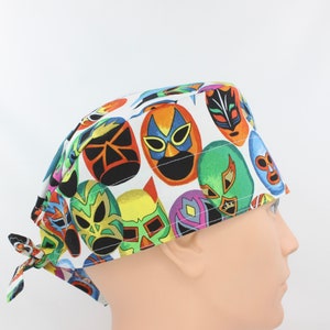 May include: A white surgical scrub cap featuring a colorful pattern of luchador masks in various colors, including orange, green, blue, and yellow. The cap has a tie closure and is designed for medical professionals or anyone needing head covering.