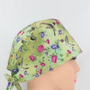 May include: Green surgical scrub hat with a floral print featuring hummingbirds and pink and purple flowers.