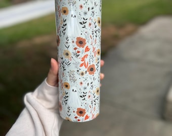 May include: A white tumbler with a floral pattern and ghost silhouettes. The flowers are orange, red, and yellow.