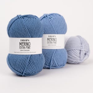 Könnte beinhalten: Zwei große Garnknäuel in Mittelblau und ein kleineres Knäuel in Hellgrau. Jedes Knäuel hat eine weiße Papierbanderole mit dem aufgedruckten Text DROPS MERINO EXTRA FINE UNI COLOUR und Superwash treated extra fine Merino wool.