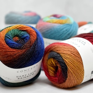 Puede incluir: Varias madejas de hilo multicolor etiquetadas como Concept by Katia Silky Lace Rainbow. El hilo presenta un degradado de colores vibrantes que incluyen rojo, naranja, amarillo, verde y azul, envueltas en bandas de papel blanco con texto negro.