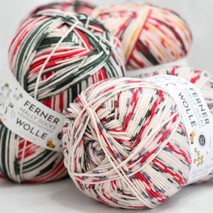 May include: Close-up of several balls of yarn with a cream, red, and green color scheme. The yarn is wrapped with a white label that has the text "FERNER MALLY SOCKS WOLLE". The yarn is suitable for knitting socks and other crafts.