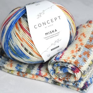Pode incluir: Uma bola de fio colorido com um rótulo branco que diz "CONCEPT by KATIA MISKA "PREMIUM SOCKS & MORE" "SOFT MERINO WOOL" 105". O fio é em um padrão multicolorido de azul, vermelho, laranja, amarelo e branco. Duas amostras de tricô do fio estão em primeiro plano.