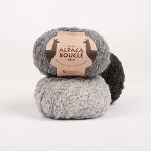 May include: Three balls of textured yarn stacked together. The top ball is light gray, the middle is a lighter gray, and the back is dark charcoal. A tan paper label wraps the top ball, featuring two llama silhouettes and the text DROPS ALPACA BOUCLÉ MIX.