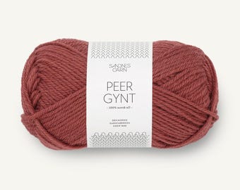 May include: A skein of dusty rose-colored yarn wrapped in a white paper label. The label features the text Sandnes Garn, Peer Gynt, 100% norsk ull, and Den Norske Garnfabrikken Siden 1888, along with a geometric chevron and knit-stitch pattern.