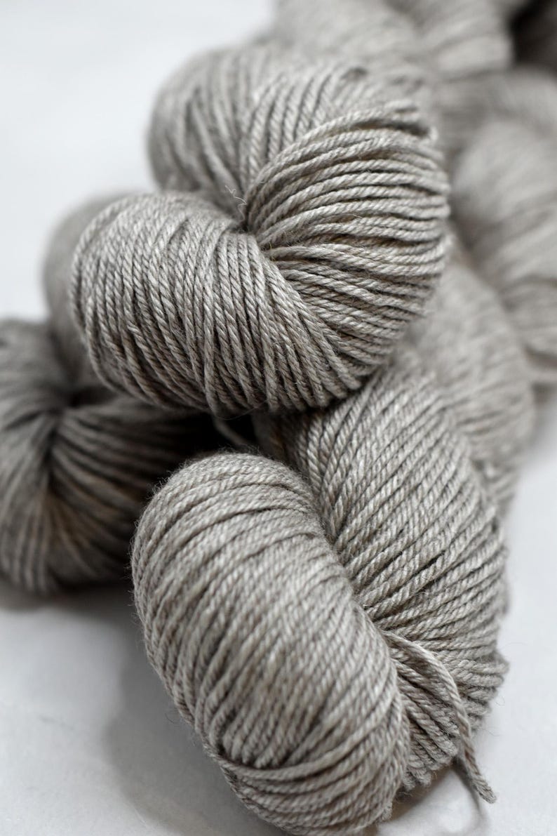 May include: Close-up of several skeins of gray yarn. The yarn is tightly wound, showing the individual strands. The color is a neutral gray, suitable for various knitting or crochet projects. The image is well-lit, highlighting the texture of the yarn.