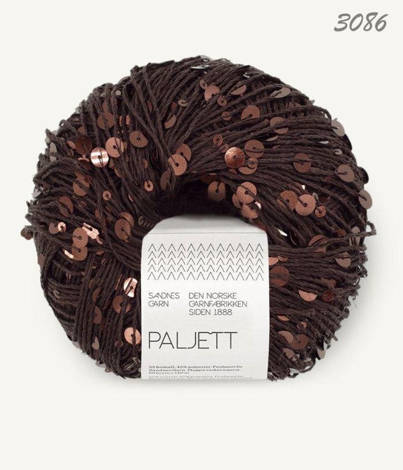 May include: A ball of dark brown yarn featuring integrated metallic copper-colored sequins throughout. A white paper label is wrapped around the center, displaying the text Sandnes Garn, Den Norske Garnfabrikken Siden 1888, and Paljett.