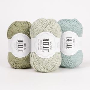 May include: Three skeins of yarn in shades of olive green, light sage green, and pale mint green. Each skein features a white paper label with the text DROPS BELLE UNI COLOUR Everyday luxury printed in black, wrapped around the centre of the yarn.