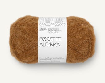 May include: A ball of fuzzy, golden-brown yarn wrapped in a white paper label. The label features the text Sandnes Garn, Den Norske Garnfabrikken Siden 1888, and Børstet Alpakka, along with technical details including 50 grams and 110 meters.