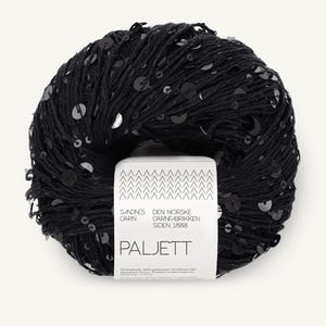 May include: A round ball of black yarn embellished with small, shiny black sequins. A white paper label is wrapped around the center, featuring the text Sandnes Garn, Den Norske Garnfabrikken Siden 1888, Paljett, and the number 1090 at the top.