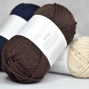 May include: Three skeins of yarn in brown, navy blue, and cream colors. The brown skein has a label that reads "Peer Gynt" and "Rilleknit".