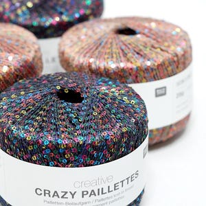 May include: Close-up of several spools of yarn covered in colorful sequins. The yarn is labeled "CRAZY PAILLETTES" and is a knit-in thread. The spools are various colors, including black, brown, and orange, with a white label.