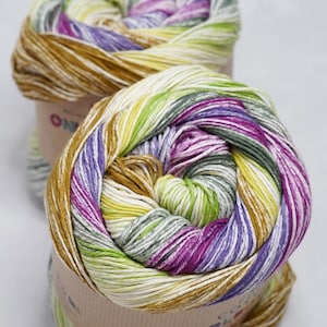 May include: Two skeins of colourful yarn. The yarn is a mix of colours including yellow, green, purple, and brown. The yarn is wrapped around a cardboard tube. The yarn is labelled with the brand name.