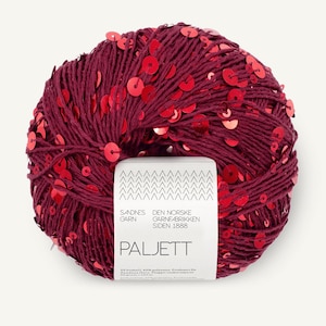 May include: A round ball of deep burgundy yarn embellished with numerous small, shiny red sequins. A white paper label is wrapped around the center, featuring the text Sandnes Garn, Den Norske Garnfabrikken Siden 1888, and Paljett.