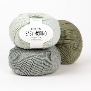 May include: Three balls of yarn stacked together. The top ball is light mint green, the bottom is heather gray, and the one behind is olive green. A white paper label on the top ball reads DROPS BABY MERINO UNI COLOUR Superwash treated extra fine Merino wool.