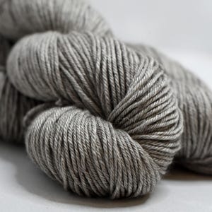 May include: Close-up of several skeins of gray yarn. The yarn is tightly wound, showing individual strands. The color is a neutral gray, suitable for various knitting or crochet projects. The yarn is soft and appears to be made of natural fibers.