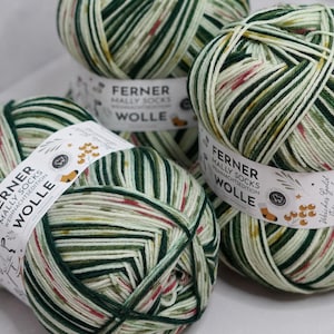May include: Three balls of Ferner Mally Socks Wolle yarn featuring a variegated colour palette of dark green, light green, cream, and small red speckles. Each ball is wrapped in a white paper label with black text and holiday-themed illustrations.