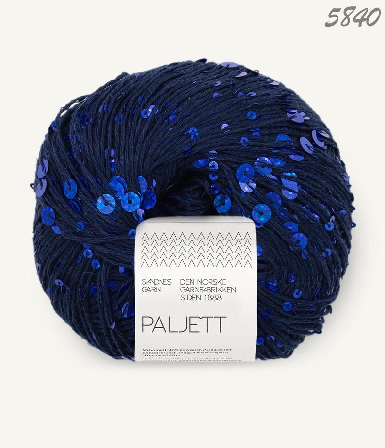 May include: A ball of dark navy blue yarn embellished with vibrant blue sequins. A white paper label is wrapped around the center, featuring the text Sandnes Garn, Den Norske Garnfabrikken Siden 1888, Paljett, and the number 5840 at the top right.