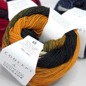 May include: Three skeins of Concept by Katia Symmetric Socks & More Degrade yarn. The front skein features a gradient of mustard yellow, olive green, and black. Each skein has a white paper label detailing 75% wool and 25% polyamide, 100g, 400m.
