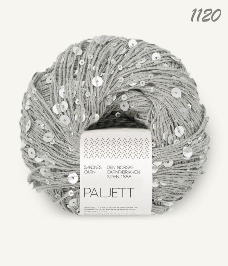 May include: A ball of light gray yarn interwoven with small, reflective silver sequins. A white paper label wraps around the center, featuring the text Sandnes Garn, Den Norske Garnfabrikken Siden 1888, Paljett, and the number 1120 at the top.