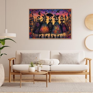 Puede incluir: Una obra de arte enmarcada representa a seis brujas con vestidos y sombreros coloridos, frente a un castillo al atardecer. Hay gatos negros a sus pies. Murci&eacute;lagos vuelan en el cielo. La obra se exhibe en una pared sobre un sof&aacute; blanco.