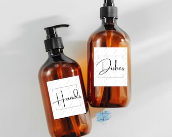 May include: Two amber glass pump bottles with white labels. The label on the left bottle says "Hands" in black cursive writing. The label on the right bottle says "Dishes" in black cursive writing.