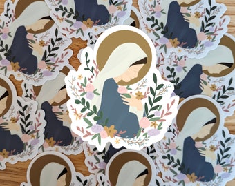 Könnte beinhalten: Ein Set mit Aufklebern, die ein religiöses Bild einer Frau in einem blauen Gewand zeigen, die ein Baby hält. Das Bild ist von einem Kranz aus Blumen und Blättern in Rosa-, Gelb- und Grüntönen umgeben.