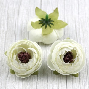 Peut inclure: Trois fleurs en tissu blanc avec un centre bordeaux. Les fleurs sont sur un fond en bois blanc.