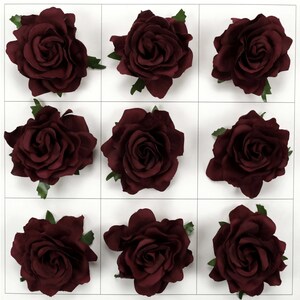 Puede incluir: Una cuadrícula de nueve cabezas de rosas artificiales en color burdeos intenso. Cada flor presenta pétalos redondeados y superpuestos dispuestos en espiral, con pequeñas hojas verdes visibles en la base de cada flor sobre un fondo blanco.