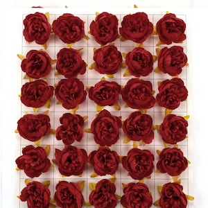 May include: A sheet of red fabric flowers arranged in a grid pattern. The flowers are all the same size and shape, and they have a slightly ruffled appearance.