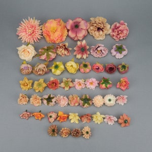May include: Assortment of artificial flowers in various colors, including pink, peach, yellow, and orange. The flowers are arranged on a gray surface, showcasing different shapes and sizes, ideal for crafting or decorative projects.