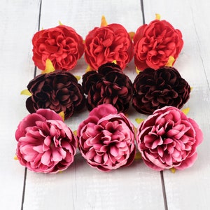 May include: Nine artificial flower heads in various shades of pink and burgundy. The flowers are arranged in a circle, with the burgundy flowers in the center and the pink flowers on the outside.