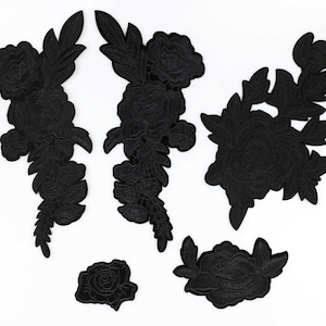 May include: A collection of six black floral embroidered patches in various sizes and designs. The patches include roses and other flower and leaf patterns, perfect for embellishing clothing or accessories. The patches are arranged on a white background.