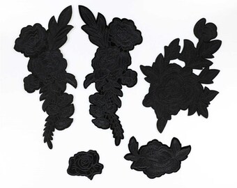 May include: A collection of six black floral embroidered patches in various sizes and designs. The patches include roses and other flower and leaf patterns, perfect for embellishing clothing or accessories. The patches are arranged on a white background.