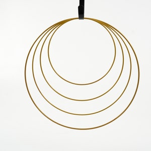 May include: A set of four gold-colored metal hoops, hanging from a black hook. The hoops are nested inside each other, creating a layered effect.