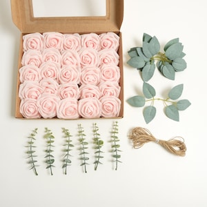 May include: A selection of craft supplies for floral arrangements. The image shows a box of light pink artificial roses, green leaves, and twine. The roses are in a cardboard box with a clear window.