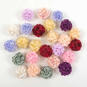 May include: Assortment of 20 small faux flower heads in various colours, including purple, pink, red, white, and cream. The flower heads are made of fabric and have a pom-pom shape.